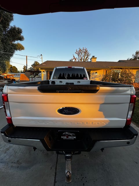 Rear view of a white Ford pickup truck parked on a residential driveway at sunset with houses visible in background