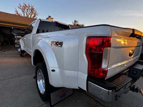White pickup truck parked at a gas station at dusk, rear three-quarter view showing truck bed and red taillights