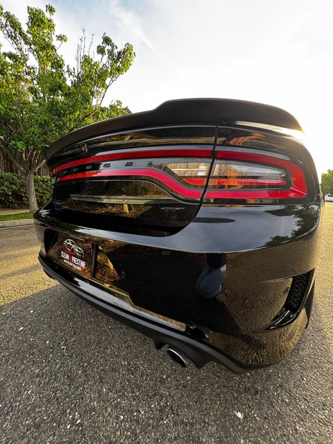 Rear view of a black convertible with red taillights and roof retracted, parked on asphalt