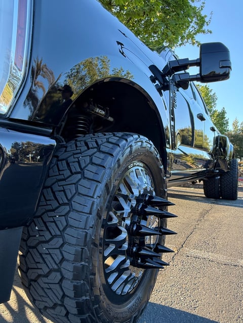 Close-up of a lifted trucks large black off-road tire with custom wheel rim in a parking lot