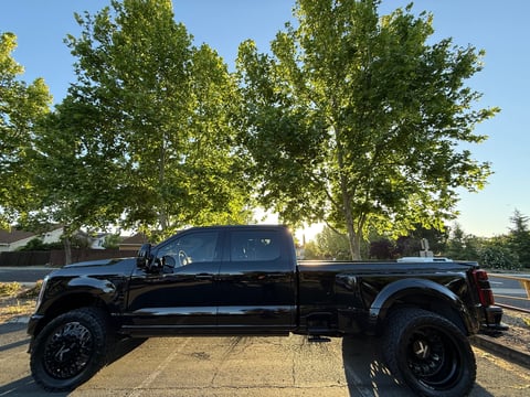 Black lifted pickup truck parked on a driveway with large green trees in the background and clear blue sky