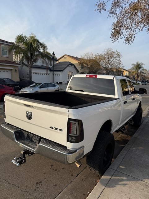 White pickup truck with open bed parked on residential street with houses and palm trees in background