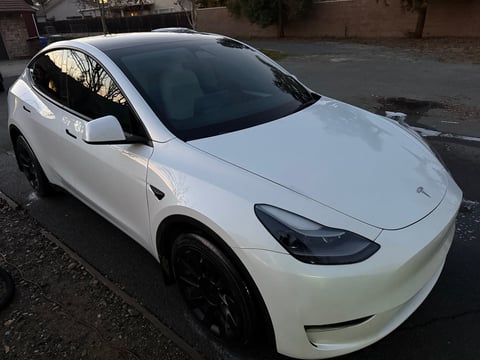 White Tesla Model Y electric vehicle parked on a street, shown from above at an angle