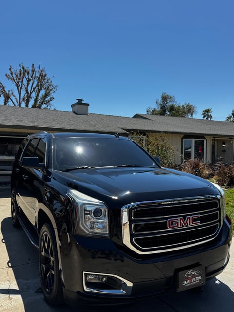 Black GMC SUV parked in driveway in front of single-story house on sunny day