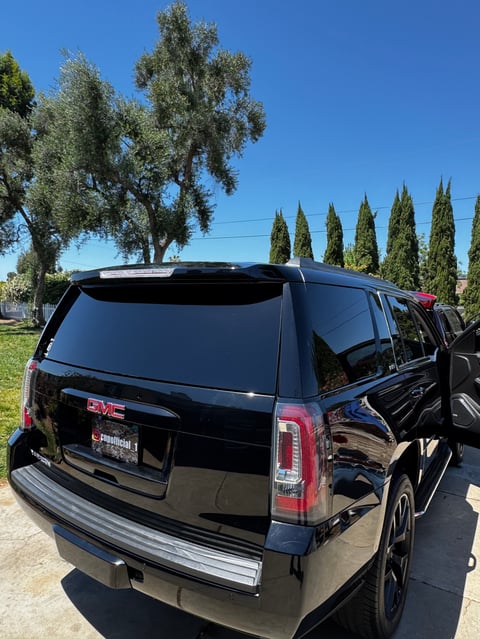Black GMC SUV parked outdoors with cypress trees and clear blue sky in background