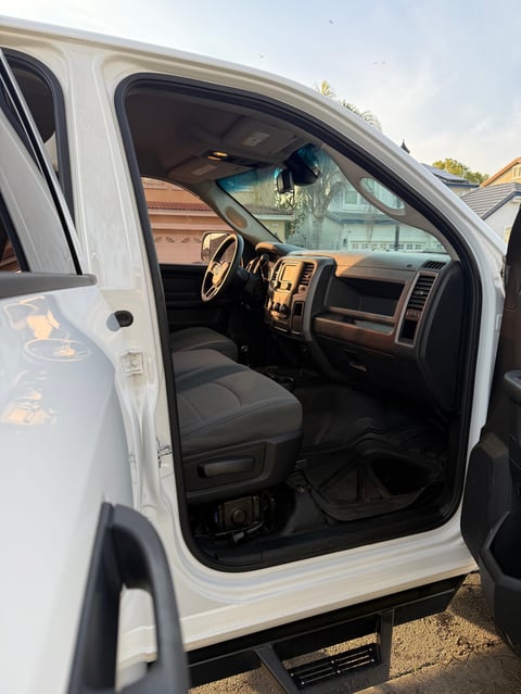 Open driver side door of white pickup truck showing interior with steering wheel, dashboard, and black seats
