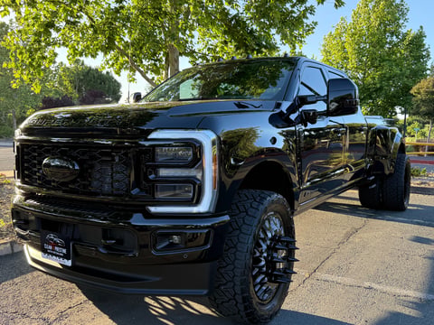 Black Ford pickup truck parked on street with green trees in background