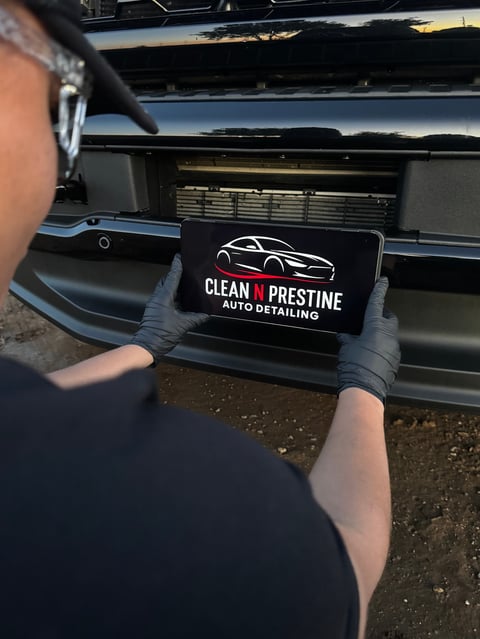 Person wearing black gloves holding a business card for Clean N Prestine Auto Detailing in front of a car